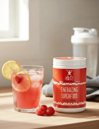 Rootz Energizing Superfood raspberry lemonade flavor with a refreshing glass of pink drink, lemon slices, fresh raspberries, shaker bottle, and gym towel on kitchen counter